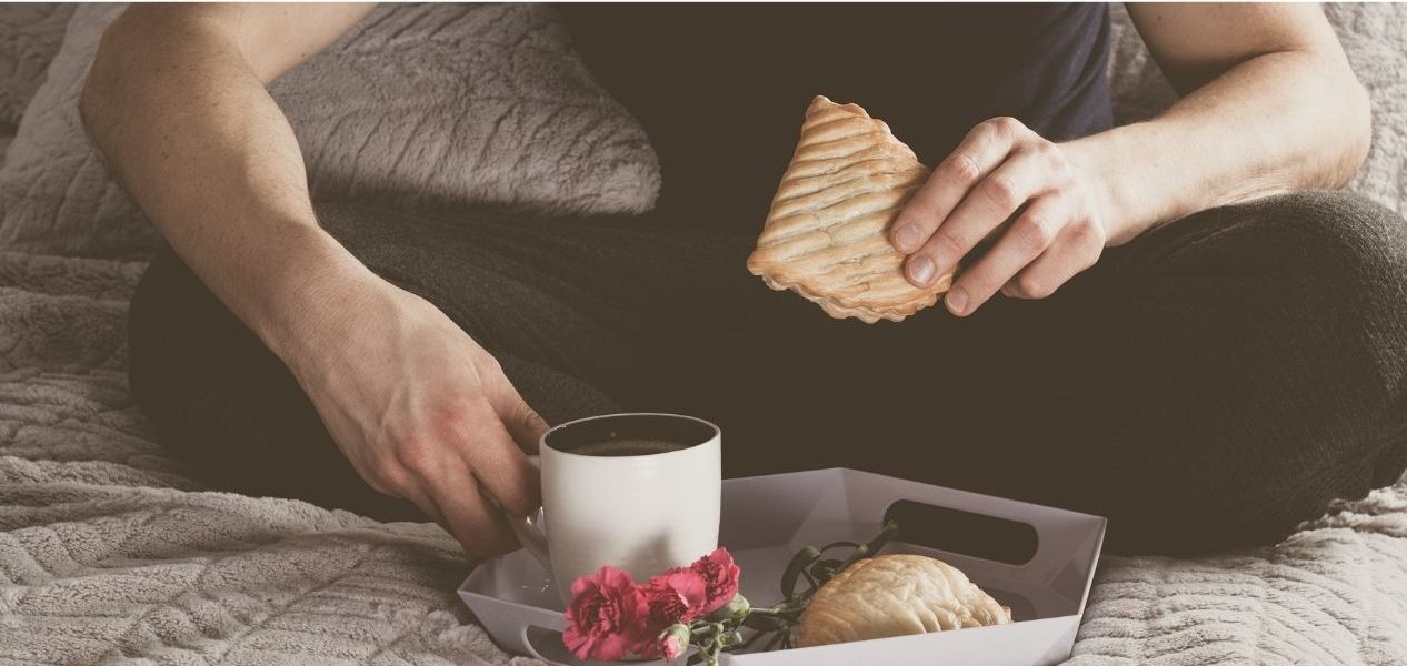 l'immagine rappresenta un uomo seduto sul letto che beve caffè e mangia un toast